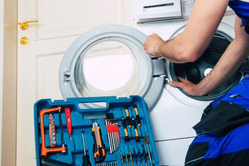 Techniker und Werkzeugkoffer vor geöffnetem Wäschetrockner.